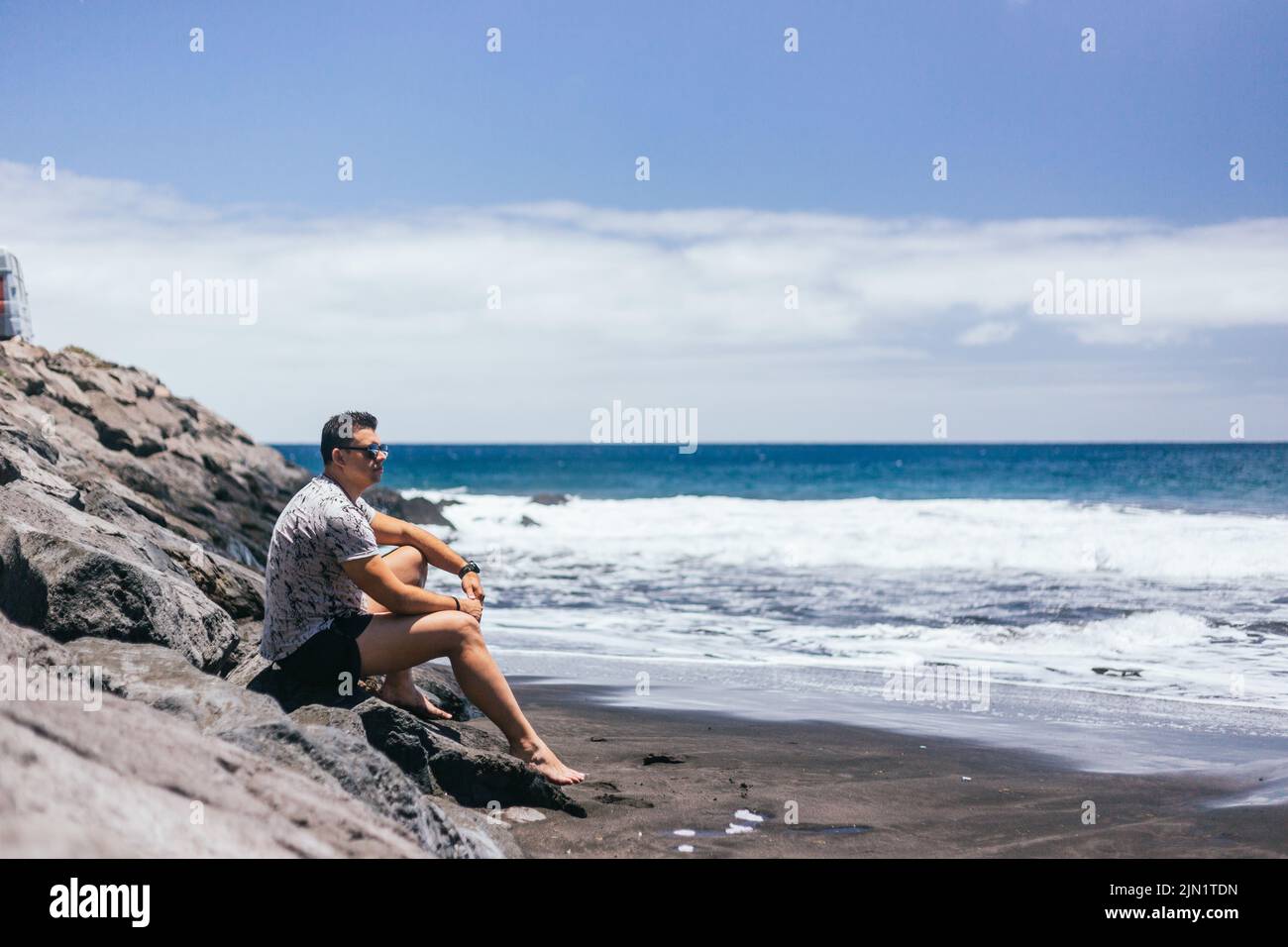 Schöner junger Mann, der am schwarzen Sandstrand spazieren geht Stockfoto