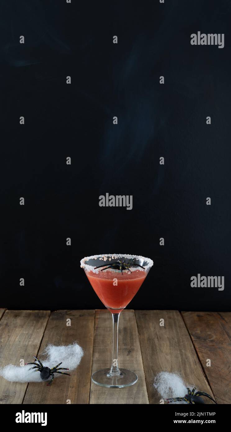 Gruseliger roter Cocktail mit Spinne auf schwarzem Hintergrund und Holztisch für Halloween. Vertikales Foto. Speicherplatz kopieren. Stockfoto
