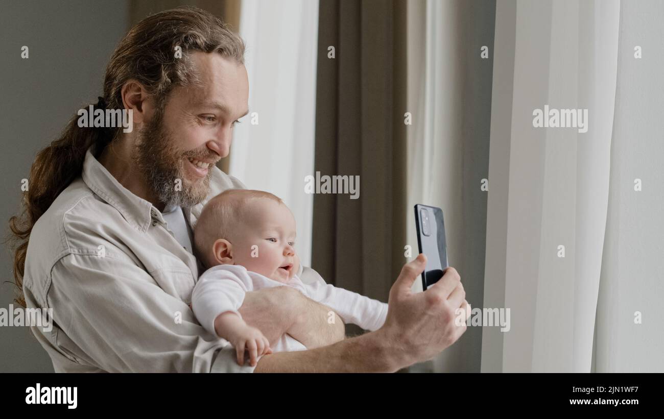 Glücklich lächelnd kaukasischen Vater Erwachsene Papa hält neugeborenes Kind zu Hause in der Nähe des Fensters Vater mit kleinen Tochter Sohn Kleinkind Neugeborenen Foto machen Stockfoto