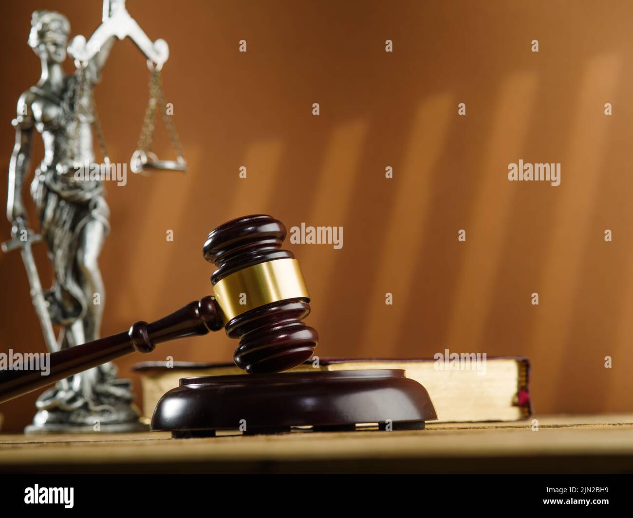 Urteilsvermögen und Gerechtigkeit. Ein hölzerner Gavel eines Richters, ein offenes Buch - die Verfassung und eine bronzene Figur der Göttin der Gerechtigkeit - Themis auf einem beigen b Stockfoto