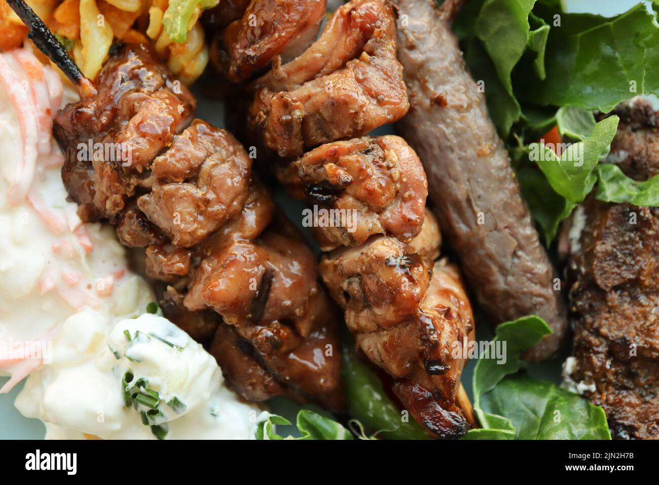 Teller mit Braai-Fleisch und Salaten. Dazu gehören Hühnerkebabs, Boerewors-Wurst, Lammkoteletts, Kartoffelsalat, Krautsalat und Curry-Nudelsalat Stockfoto