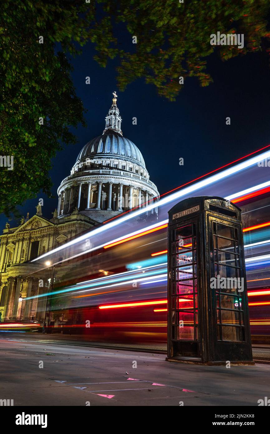 London, Großbritannien - 11. Juni 2022: Leichte Wege eines roten Doppeldeckerbusses hinter einer schwarzen Telefonzelle mit der Kuppel der St. Paul's Cathedral im Hintergrund Stockfoto