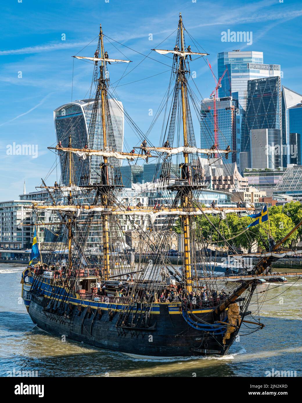 Das schwedische Segelschiff Göteborg, das sich in Richtung Tower Bridge aufmacht, mit Crew im Takeling, vor dem Hintergrund der Hochhäuser der City of London. Stockfoto