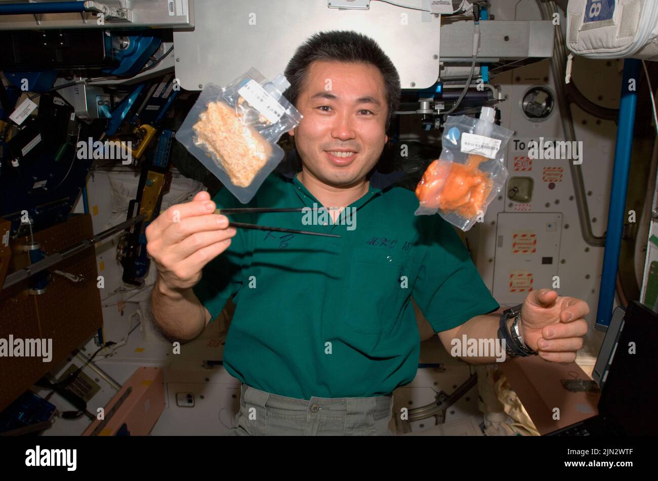 ISS - 03. Juni 2009 - der Astronaut der Japan Aerospace Exploration Agency (JAXA), Koichi Wakata, Flugingenieur der Expedition 20, hält Essstäbchen in der Nähe von zwei Lebensmitteln Stockfoto