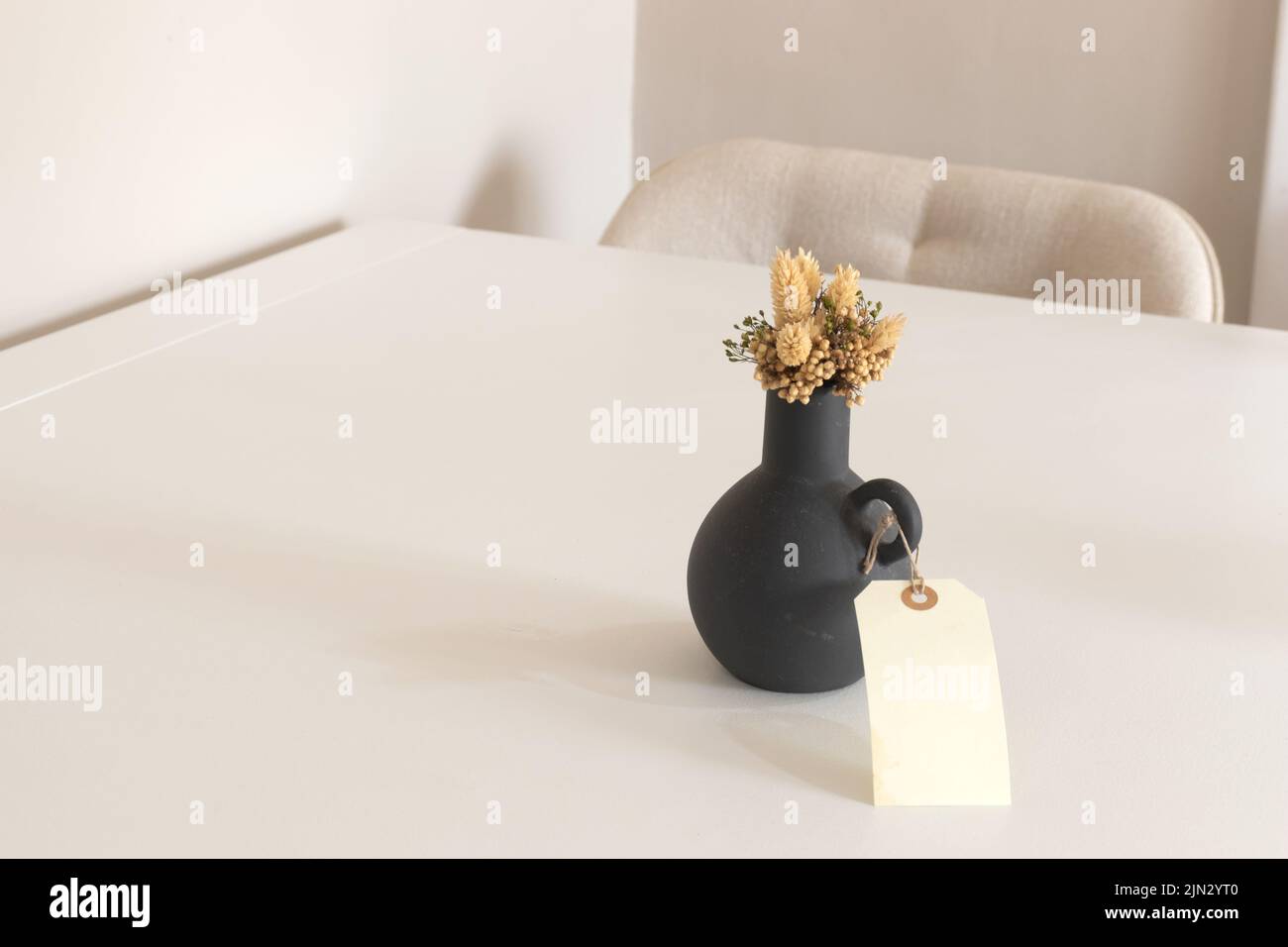 Innenhintergrund des modernen leeren Raumes mit weißer Wand, schwarzer Vase mit trockener Blume und Holztisch, Kopierraum. Stockfoto