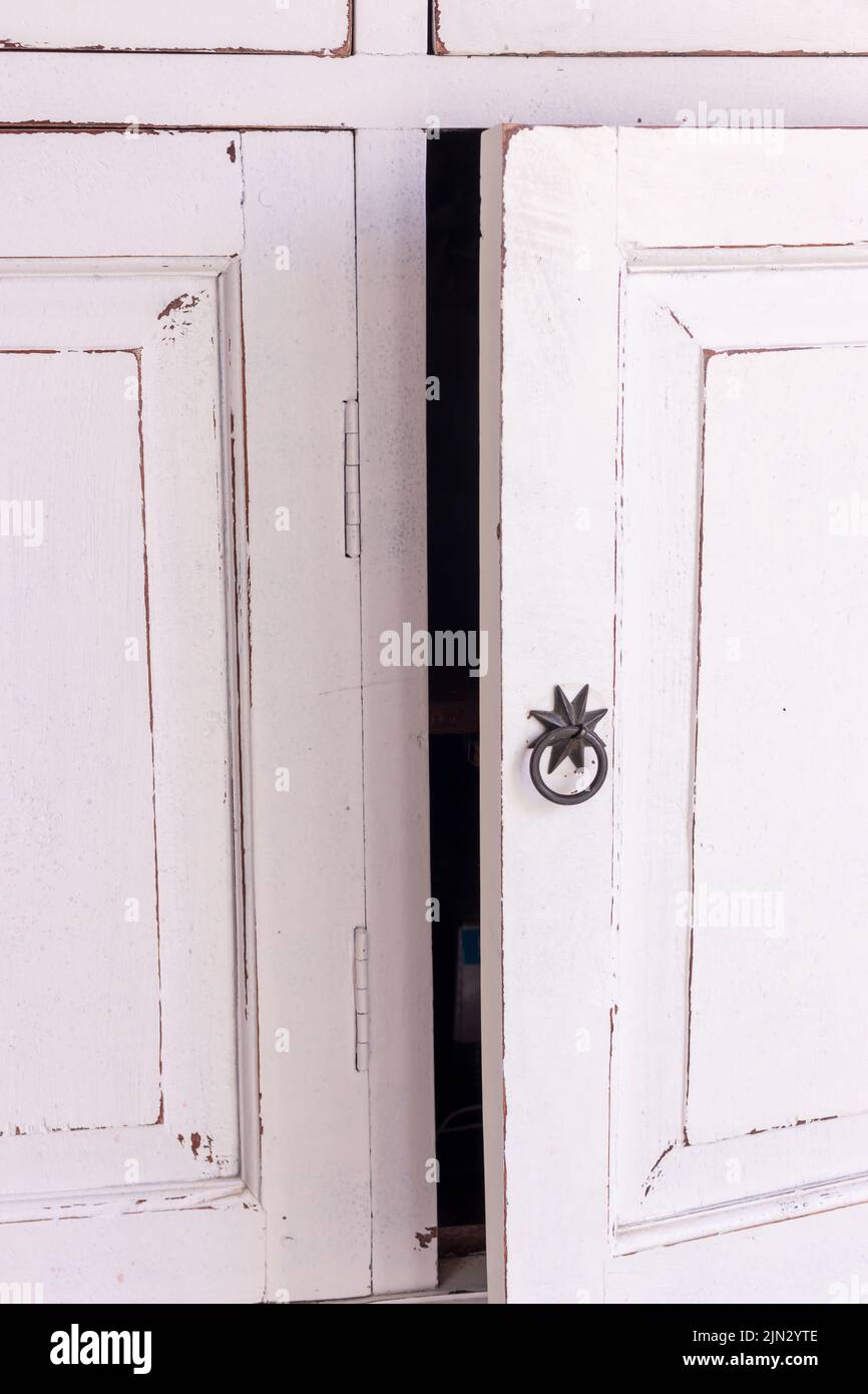 Ajar Schranktür. Weißer, frisch bemalter antiker Schrank mit halb geöffneter Tür. Stockfoto