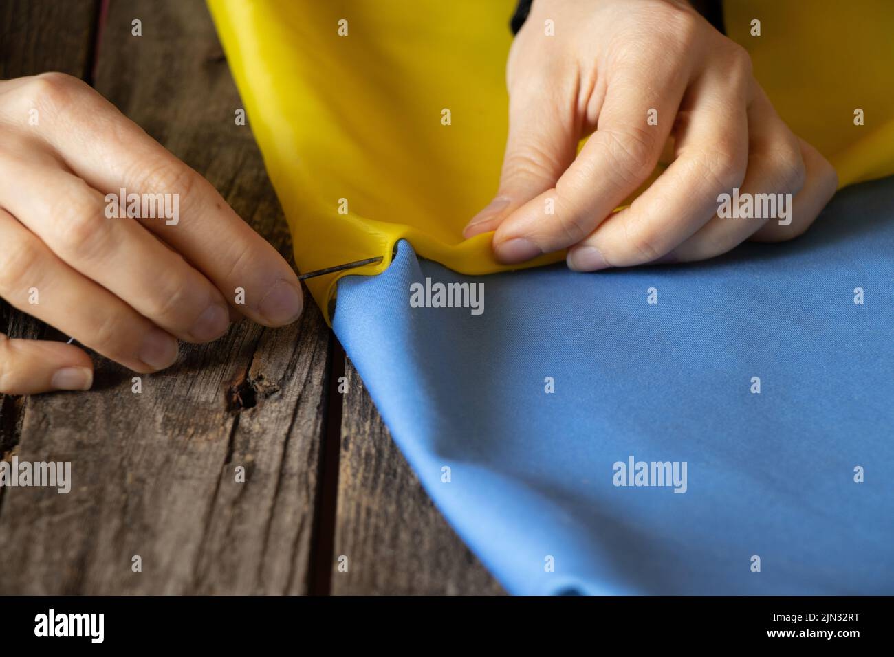 Frauenhände nähen die Nationalflagge der Ukraine gelb-blau am Tisch zu Hause in der Ukraine, Patriot, stoppen den Krieg in der Ukraine 2022 Stockfoto