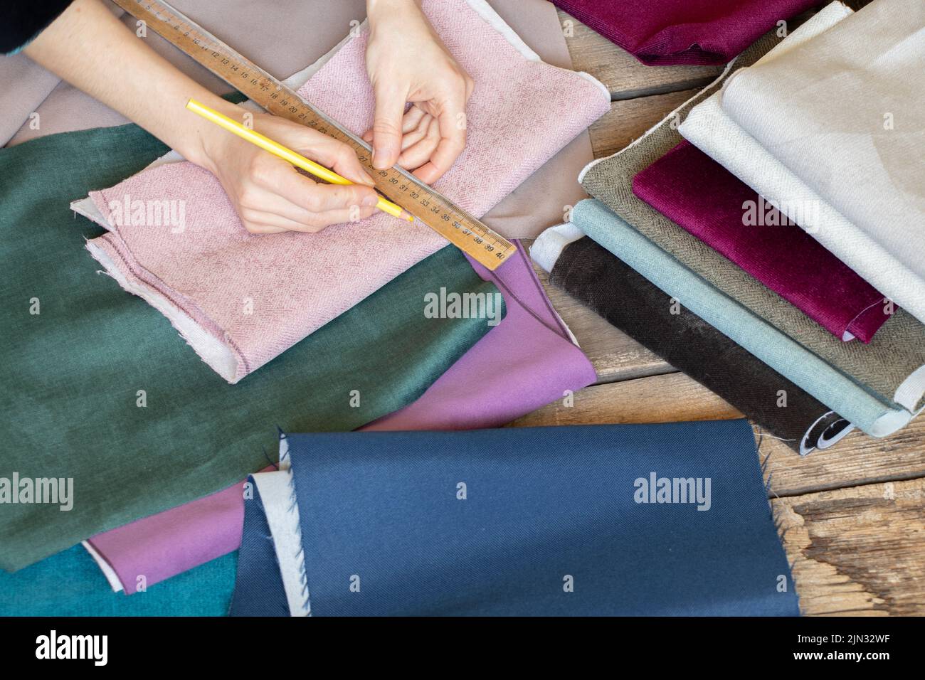 Weibliche Hände schneiden verschiedene Stoffstücke auf dem Tisch, Schneiderwerkstatt, Nähen und Mode, Schneiderei Stockfoto