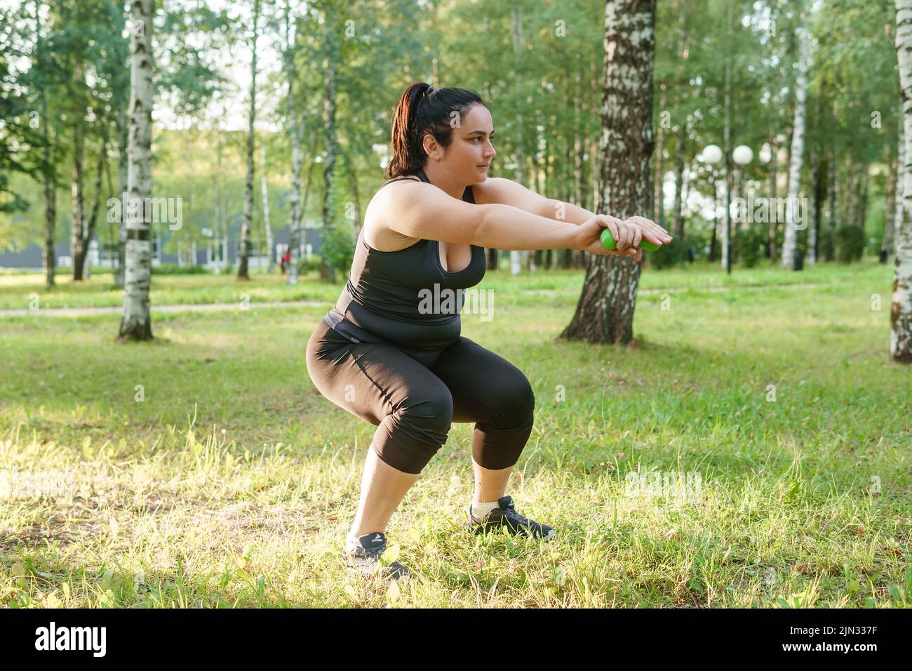 Eine charmante Brünette Frau plus-Größe Körper positiv praktiziert Sport in der Natur. Übungen mit Kurzhanteln. Stockfoto