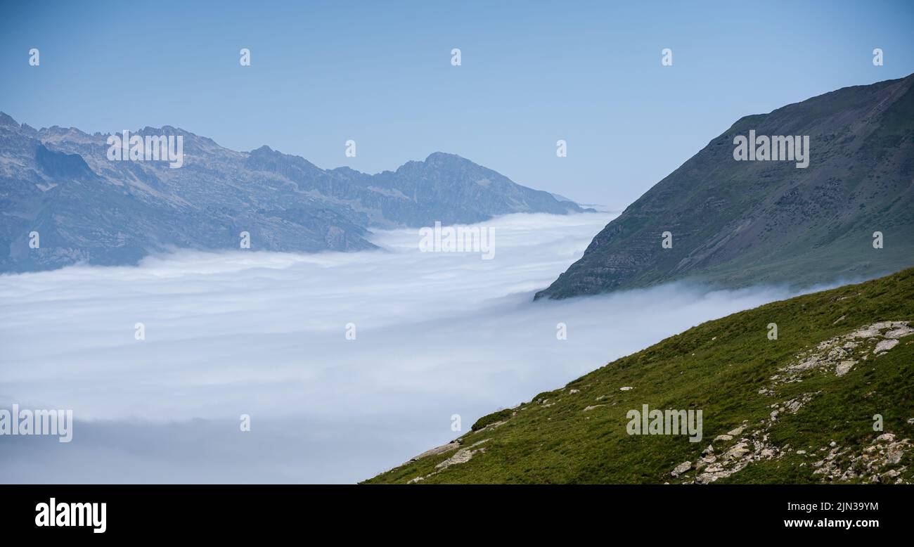 Ein riesengroßes, kreisförmiges Tal, umgeben von hohen Bergen, dem Cirque de Troumouse (Pyrenäen), Wolken, die das Tal füllen, und einem klaren, blauen Sommerhimmel Stockfoto