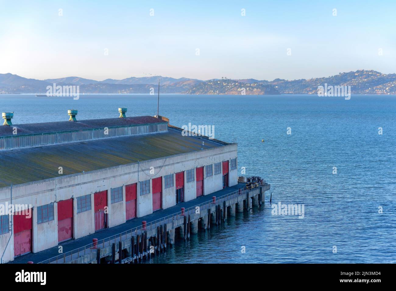 Lagerhaus am Pier in Fisherman's Wharf in San Francisco, Kalifornien. Altes Lagerhaus mit roten Toren gegen den Blick auf die Bucht und die Berge. Stockfoto