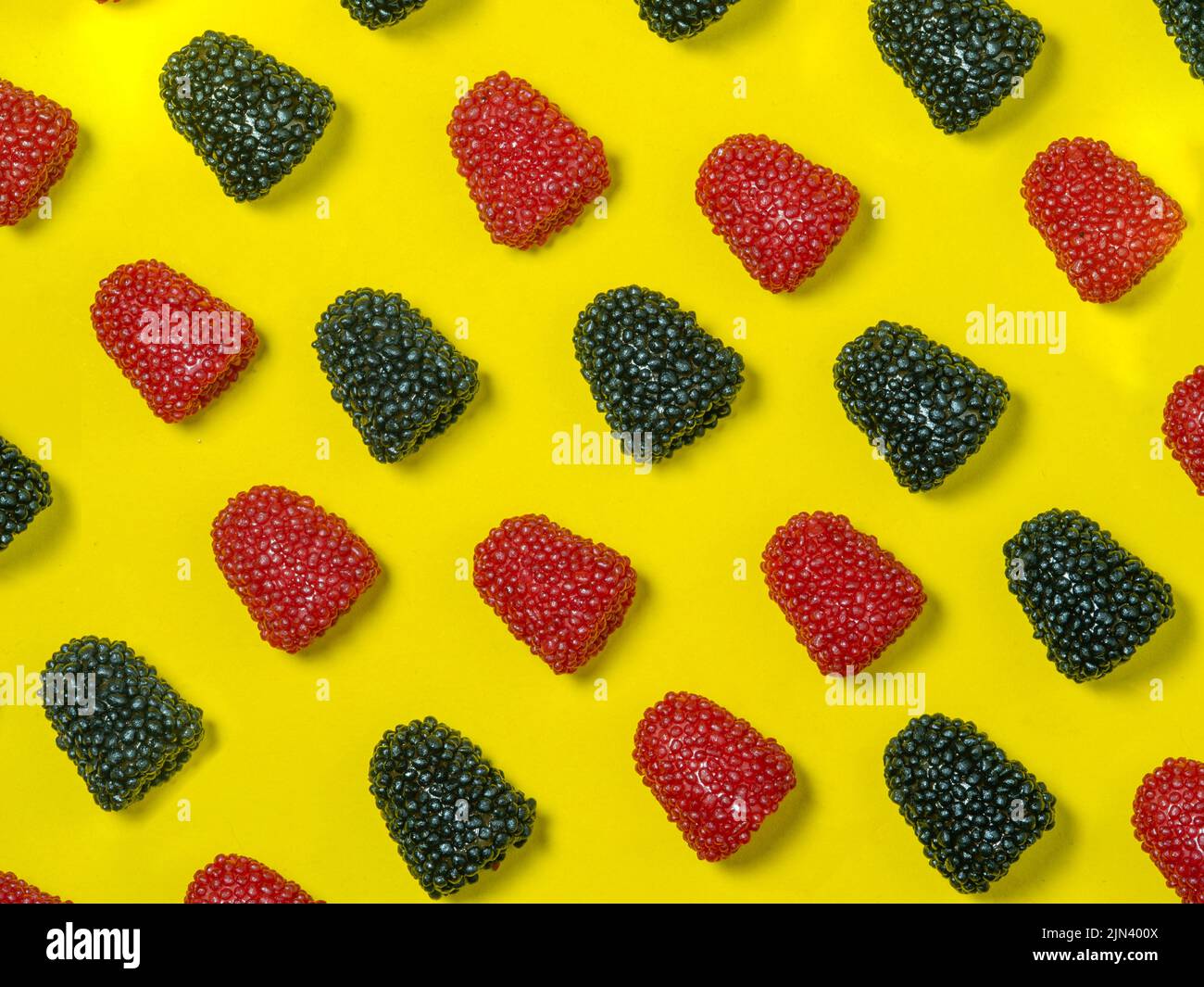 Hintergrund von roten und schwarzen Kaukwels in Form von Beeren auf gelbem Hintergrund. Süßigkeiten in Form von Himbeeren . Marmelade isolieren. In Scheiben Geschnitten Stockfoto