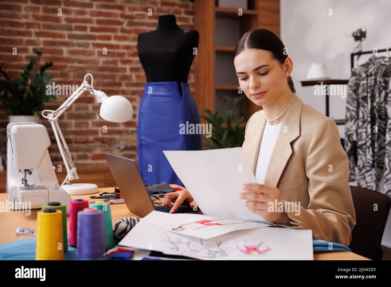 Ein junges Mädchen ist Modedesignerin, zeichnet eine Skizze vor dem Hintergrund einer Schaufensterpuppe und einer Nähmaschine, in ihrem gemütlichen Büro Stockfoto