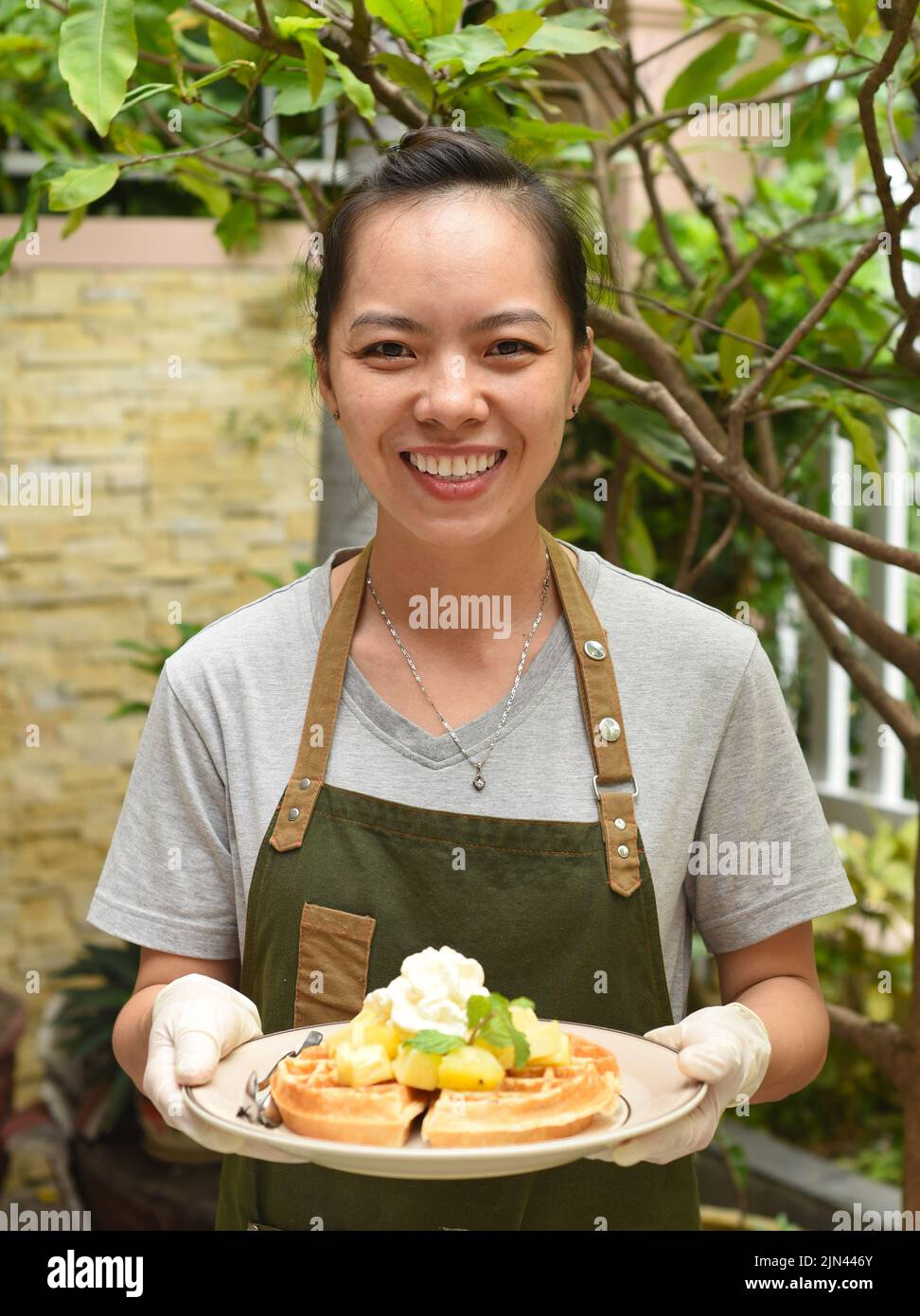 Die vietnamesische Kellnerin serviert belgische Waffeln mit Obst und Eis im Café im Freien Stockfoto