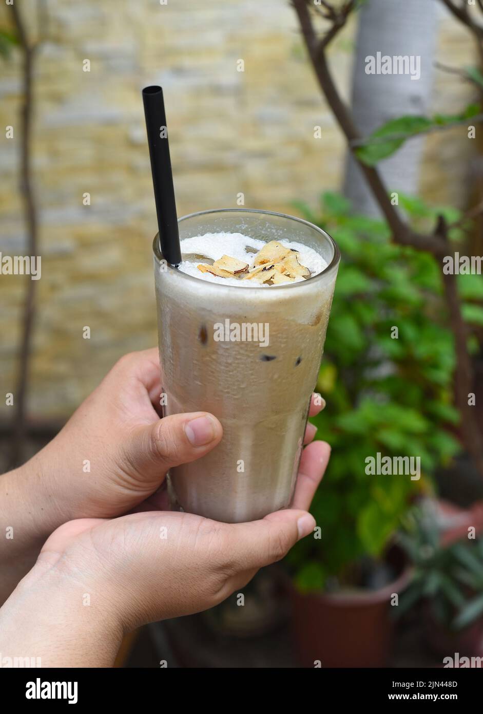 Hände halten Glas mit Kaffee Milch schütteln mit verbrannter Kokosnuss Stockfoto