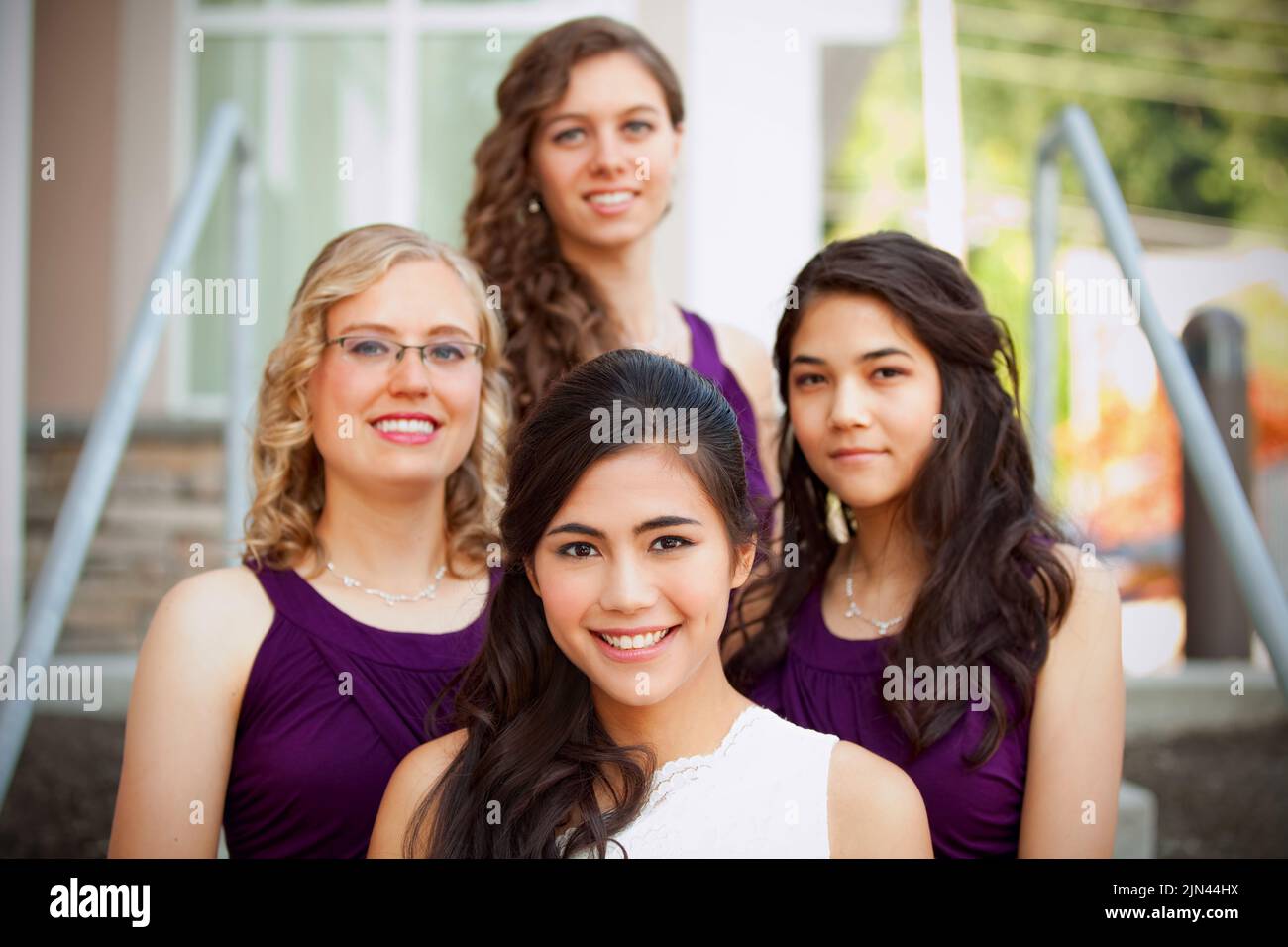 Schöne biracial junge Braut lächelt mit ihrer multiethnischen Gruppe von Brautjungfern in lila Kleidern Stockfoto