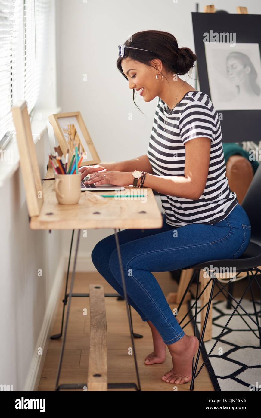 Technologie ermöglicht es Ihnen, ohne Grenzen zu schaffen. In voller Länge eine attraktive und künstlerische junge Frau, die während der Arbeit in ihrem Inneren einen Laptop benutzt Stockfoto