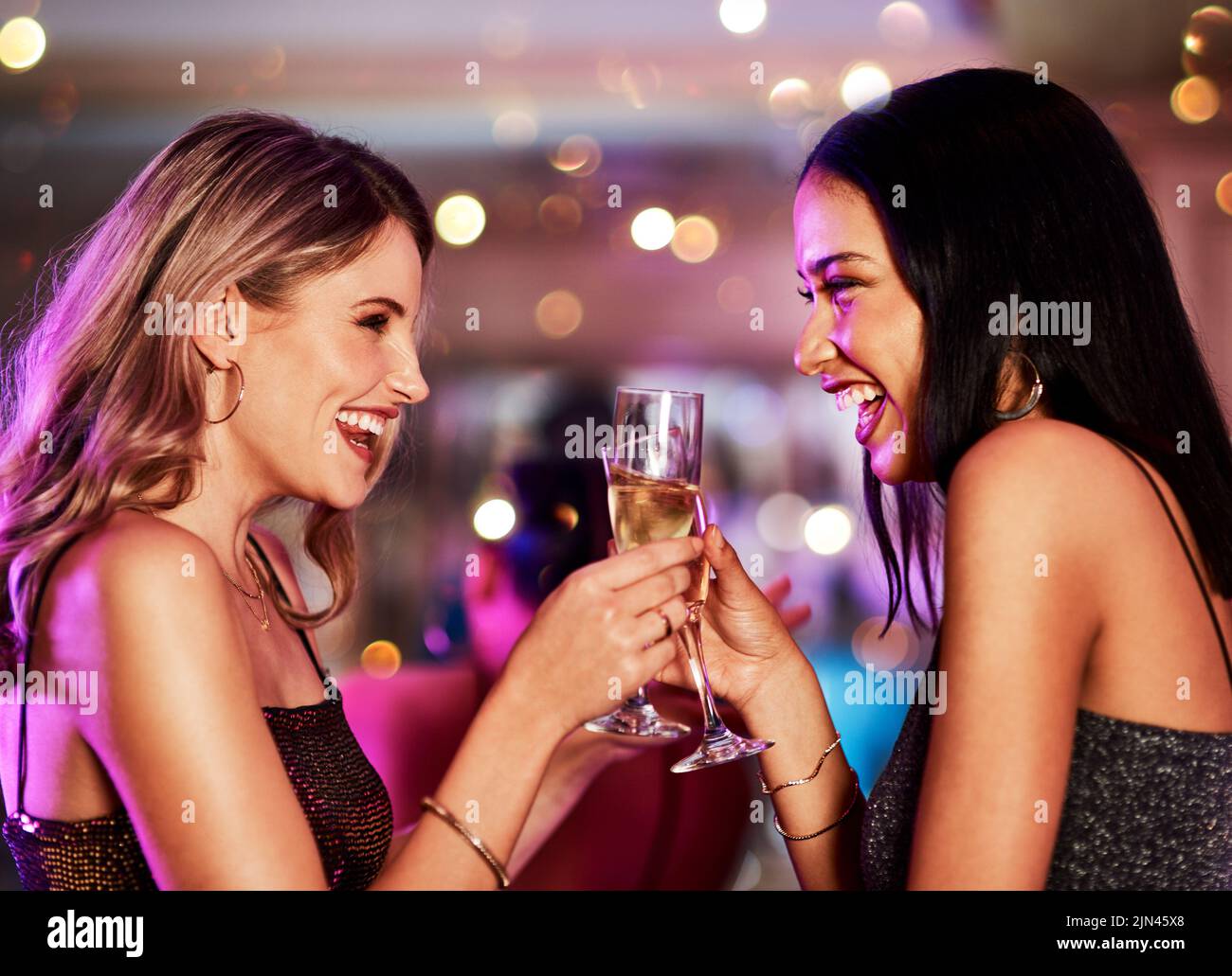 Hier geht es zu unserem zweiten. Zwei fröhliche junge Frauen, die abends mit Getränken in einer Bar einen festlichen Toast machen. Stockfoto