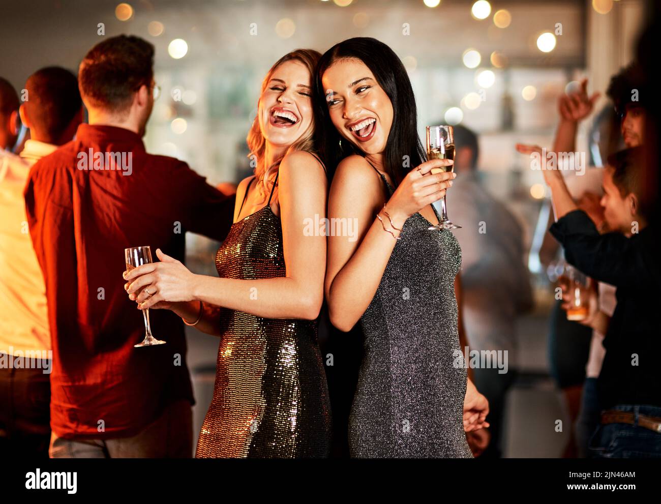 Zwei fröhliche junge Frauen, die abends auf der Tanzfläche eines Clubs tanzen und dabei einen Drink zu sich nehmen. Stockfoto