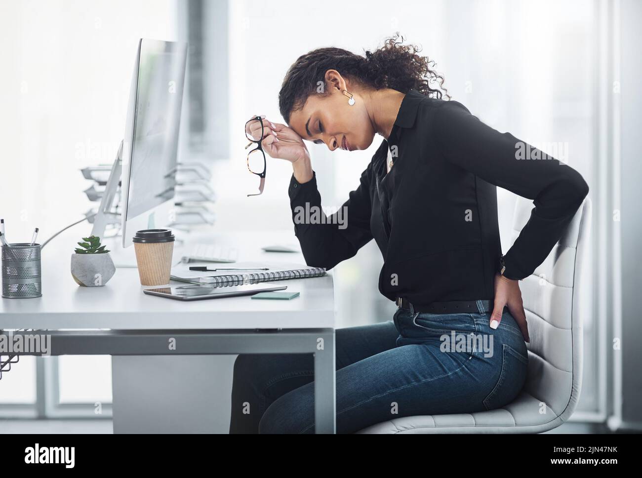 Meine Rückenschmerzen erhöhen nur meinen Stress. Eine junge Geschäftsfrau leidet mit Rückenschmerzen in einem Büro. Stockfoto