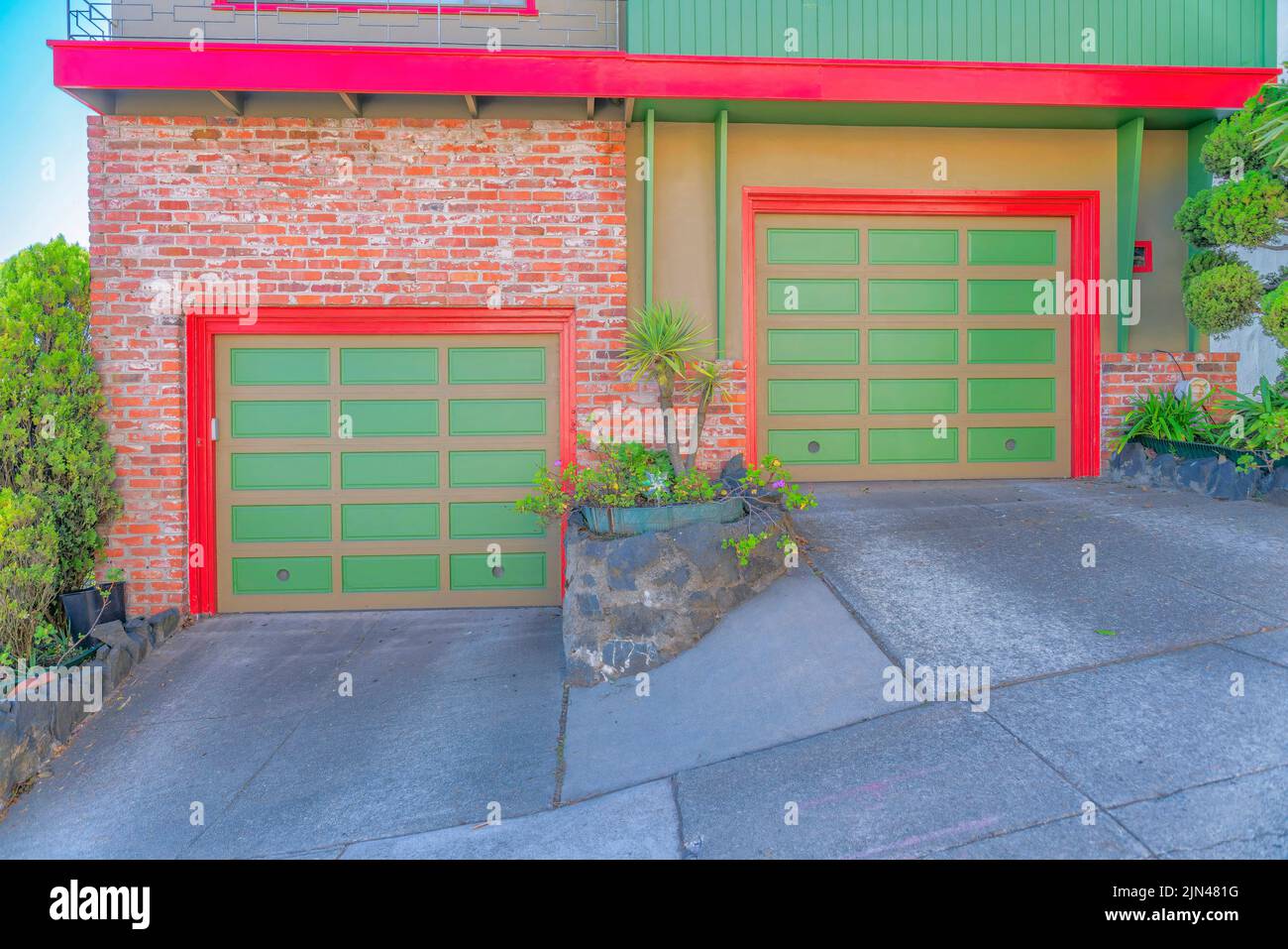 Zwei Garagentore auf einer schrägen Betonstraße in San Francisco, Kalifornien. Zwei Stadthäuser mit den gleichen Garagentoren, roten Verkleidungen und Ziegelwänden auf t Stockfoto