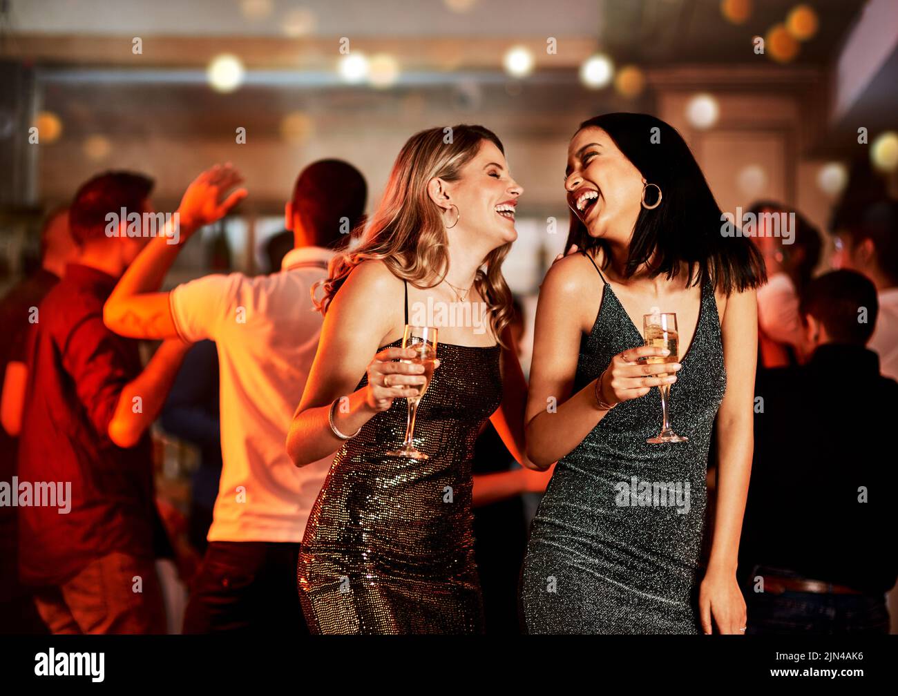 Eine tolle Nacht. Zwei fröhliche junge Frauen trinken, während sie auf der Tanzfläche eines Clubs in der Nacht tanzen. Stockfoto