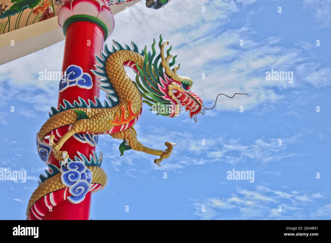 Goldene fliegende majestätische asiatische chinesische Drachenstatue mit roter Betonwand und blauem Himmel an sonnigen Tagen Stockfoto