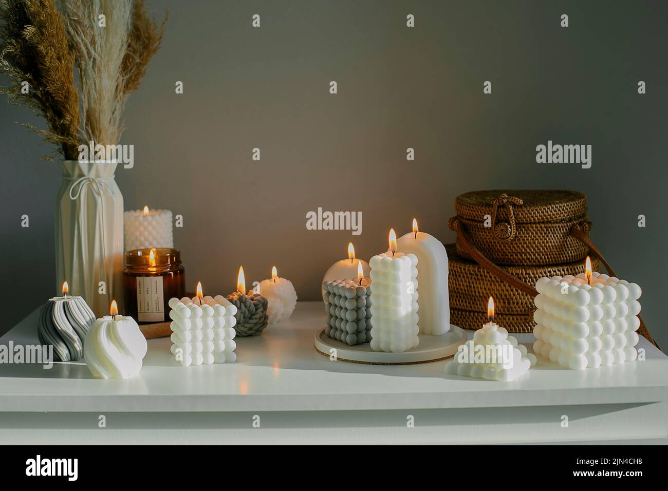 Inneneinrichtung. Weiße Kommode mit getrockneten Blumen in Vase, Rattan-Taschen und Kerzen. Stillleben, Hygge-Konzept Stockfoto