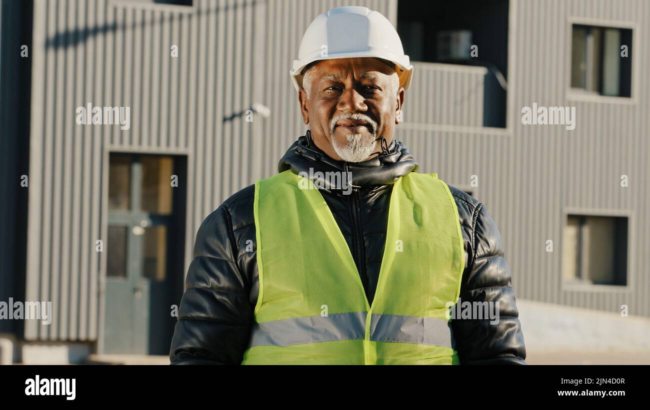 Nahaufnahme älterer afroamerikanischer Bauarbeiter, der in Schutzhelm-Uniform im Freien stand, selbstbewusster Arbeiter kreuzte die Arme über die Brust Stockfoto
