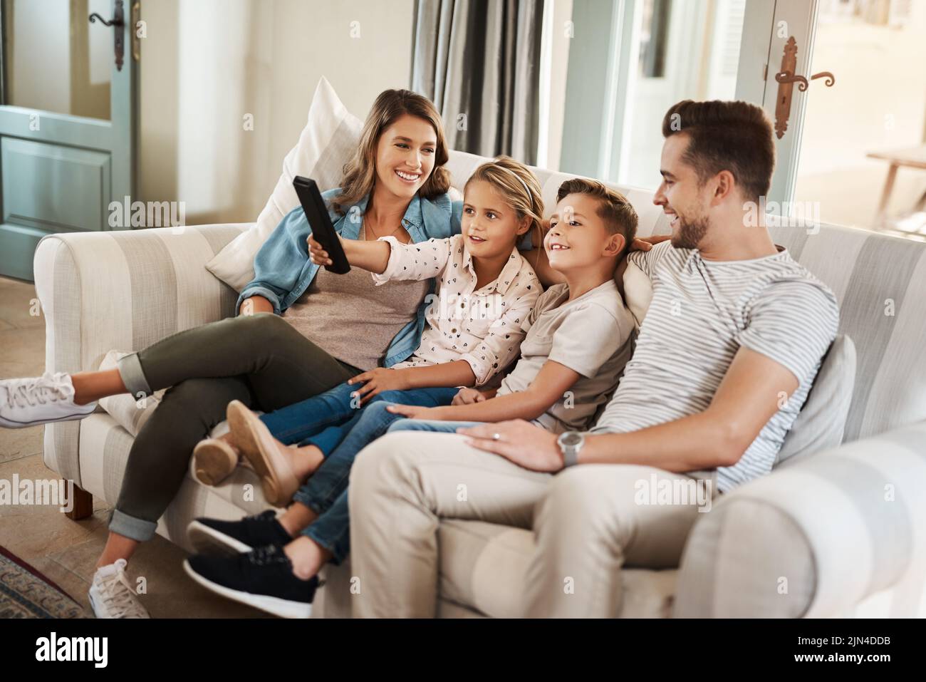 Am Wochenende ist Zeit für die Familie. Eine glückliche junge Familie, die sich auf dem Sofa entspannt und zu Hause gemeinsam fernsieht. Stockfoto