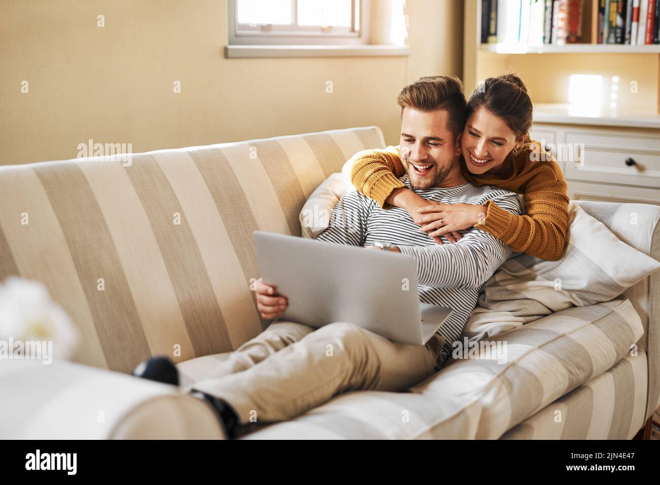 Sie teilen eine starke Verbindung. Ein junges Paar, das einen Laptop benutzt, während es sich zu Hause entspannt. Stockfoto