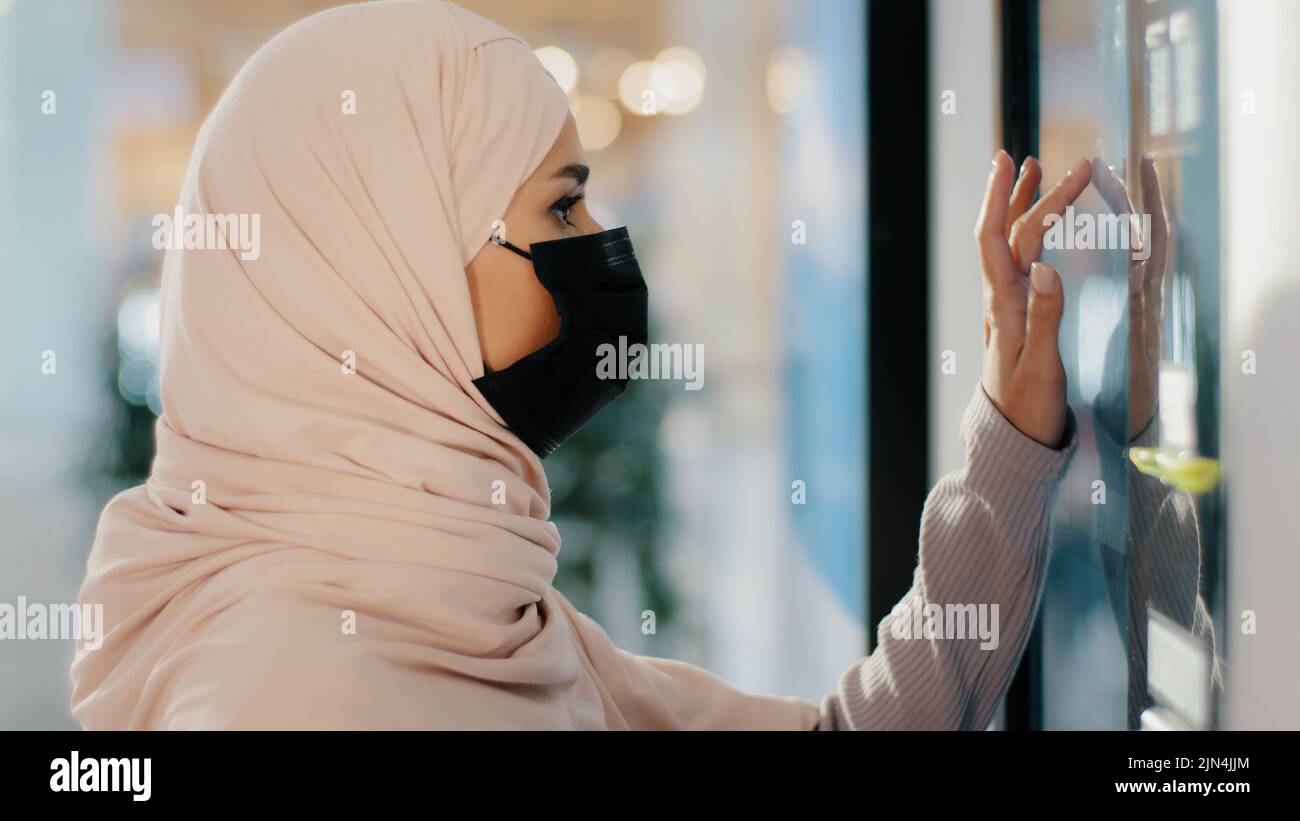 Junge arabische Frau in schützender medizinischer Maske steht in der Nähe Selbstbedienungsmaschine muslim girl Shopping bestellt Lebensmittel erhält Paket zahlt für Service Stockfoto