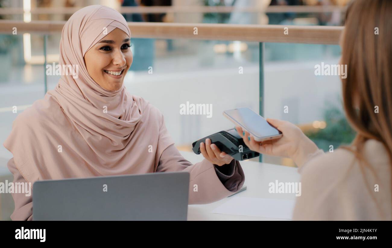 Freundliche muslimische Frau in Hijab Verkäuferagent bietet Bezahlung für Service über Bank-Terminal Mädchen Käufer Verbraucher zahlt für den Kauf mit kontaktlos Stockfoto