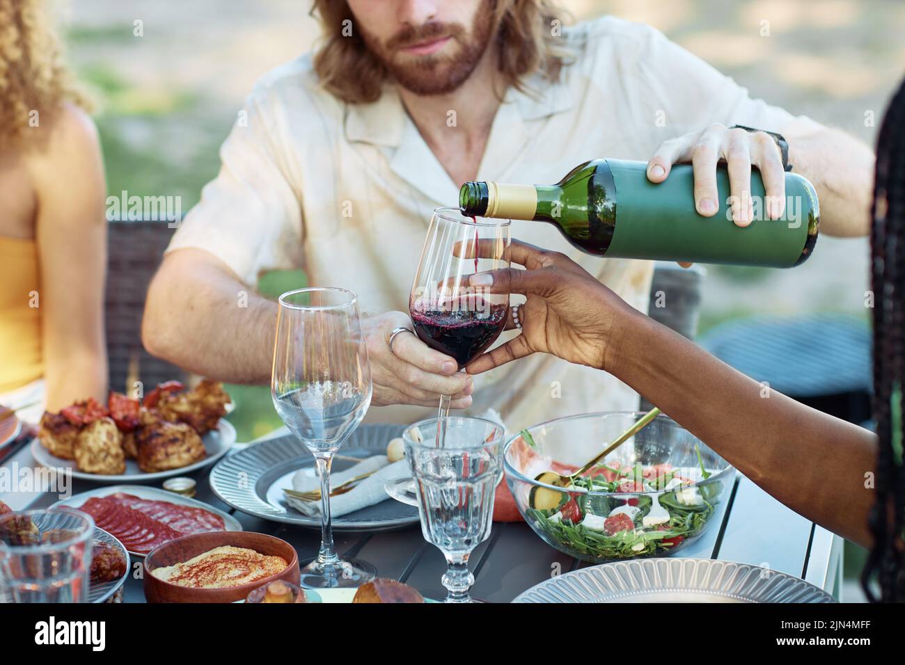 Nahaufnahme eines Paares, das im Sommer Rotwein ins Glas gießt, während es eine Dinnerparty mit Freunden im Freien genießt Stockfoto