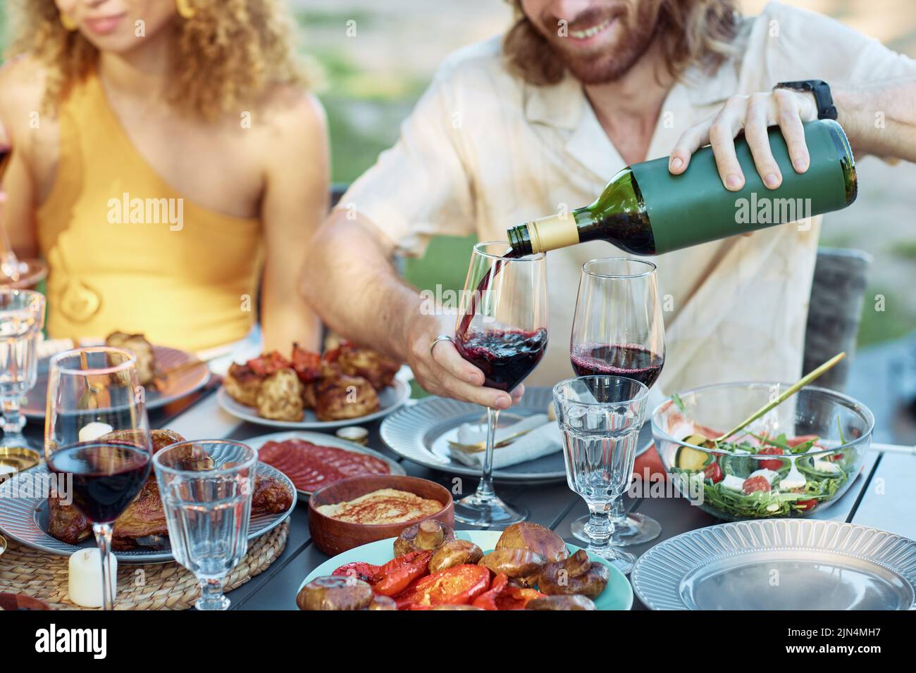 Nahaufnahme eines Mannes, der im Sommer Rotwein ins Glas gießt, während er eine Dinnerparty mit Freunden im Freien genießt Stockfoto