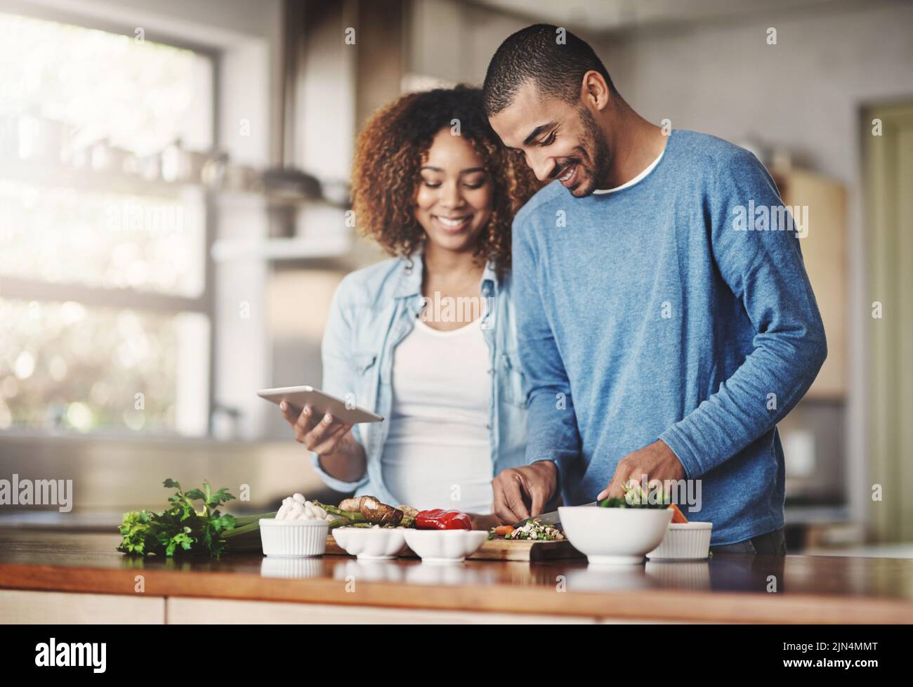 Junges, glückliches und romantisches Paar, das gemeinsam gesunde Lebensmittel kocht und Rezepte online auf einem Tablet verfolgt. Lächelnder Ehemann und Ehefrau beim Abendessen oder Mittagessen Stockfoto