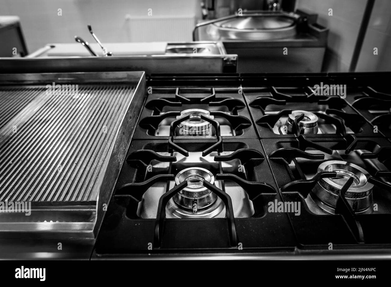 Schwarz-Weiß-Details mit geringer Schärfentiefe (selektiver Fokus) mit einem brandneuen, ungenutzten, professionellen metallischen Gasbrenner in einer Restaurantküche. Stockfoto