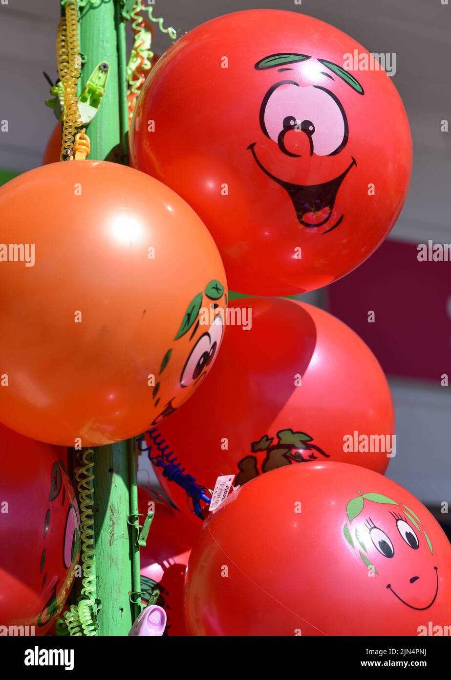 Leuchtend rote und orangefarbene Luftballons mit lächelnden Gesichtern, die am Meer zum Verkauf stehen. Stockfoto