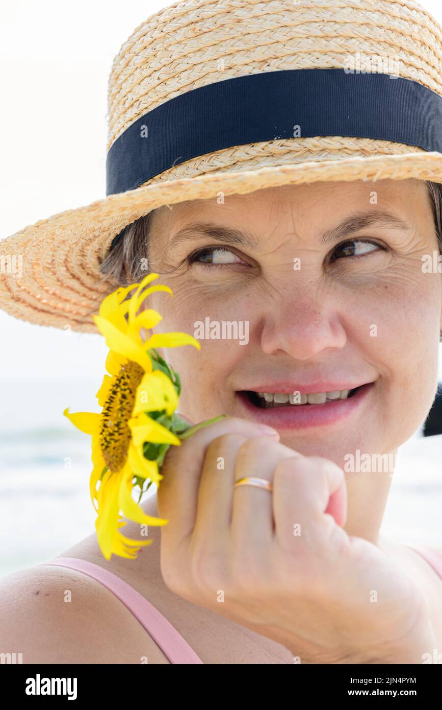 Verheiratete Frau in einem Bootsfahrer mit einer Sonnenblume in der Hand, die mit einem kleinen Lächeln spielerisch wegschaut. Urlaubskonzept. Stockfoto