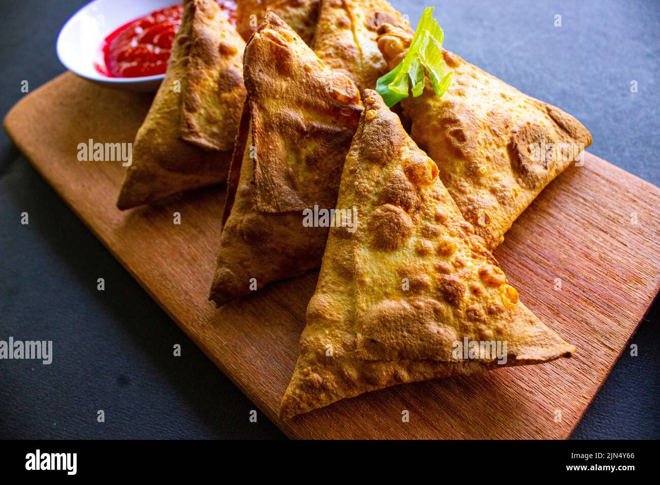 Samosa, samsa oder Somsa sind dreieckige frittierte Backwaren oder Pastri, die mit Tomatensauce und Porree-Scheibe auf schwarzem Hintergrund serviert werden Stockfoto