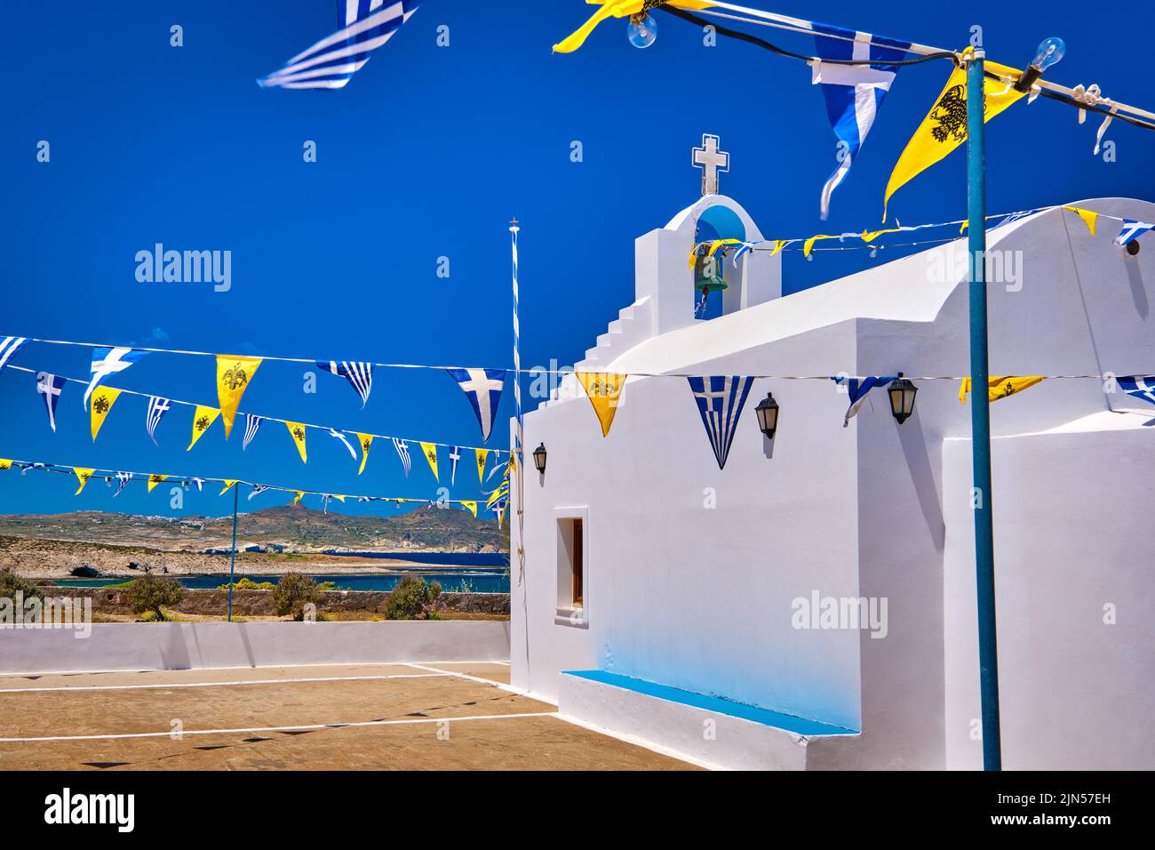 Weiße griechisch-orthodoxe Kapelle oder Kirche auf dem Hügel gegen klaren blauen Himmel an sonnigen Tagen, dekoriert griechische nationale, griechisch-orthodoxe Flagge. Milos, Griechenland Stockfoto