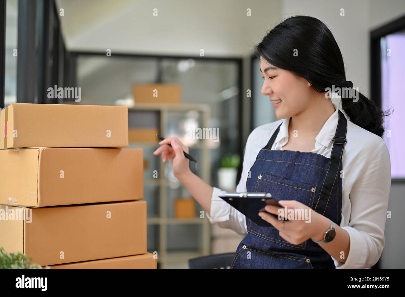 Professionelle junge asiatische Geschäftsfrau oder weibliche Online-E-Commerce-Shop-Besitzer Überprüfung ihrer Versand Tracking-Nummer, arbeiten und Vorbereitung Paket-Box Stockfoto