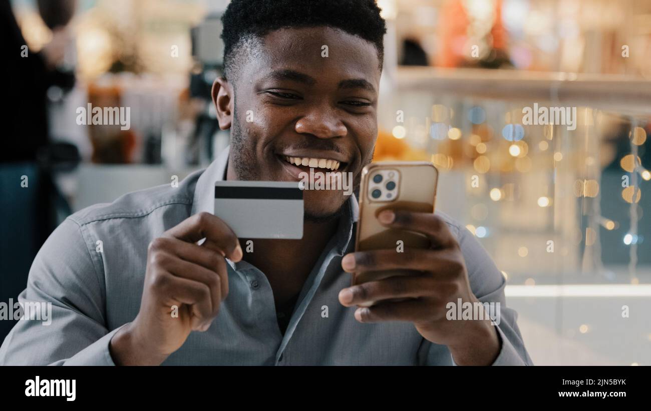 Zufriedener afroamerikanischer Mann macht Kauf im Online-Shop zahlt für Waren mit Kreditkarte auf dem Handy nutzt E-Banking-Anwendung glücklich jung Stockfoto