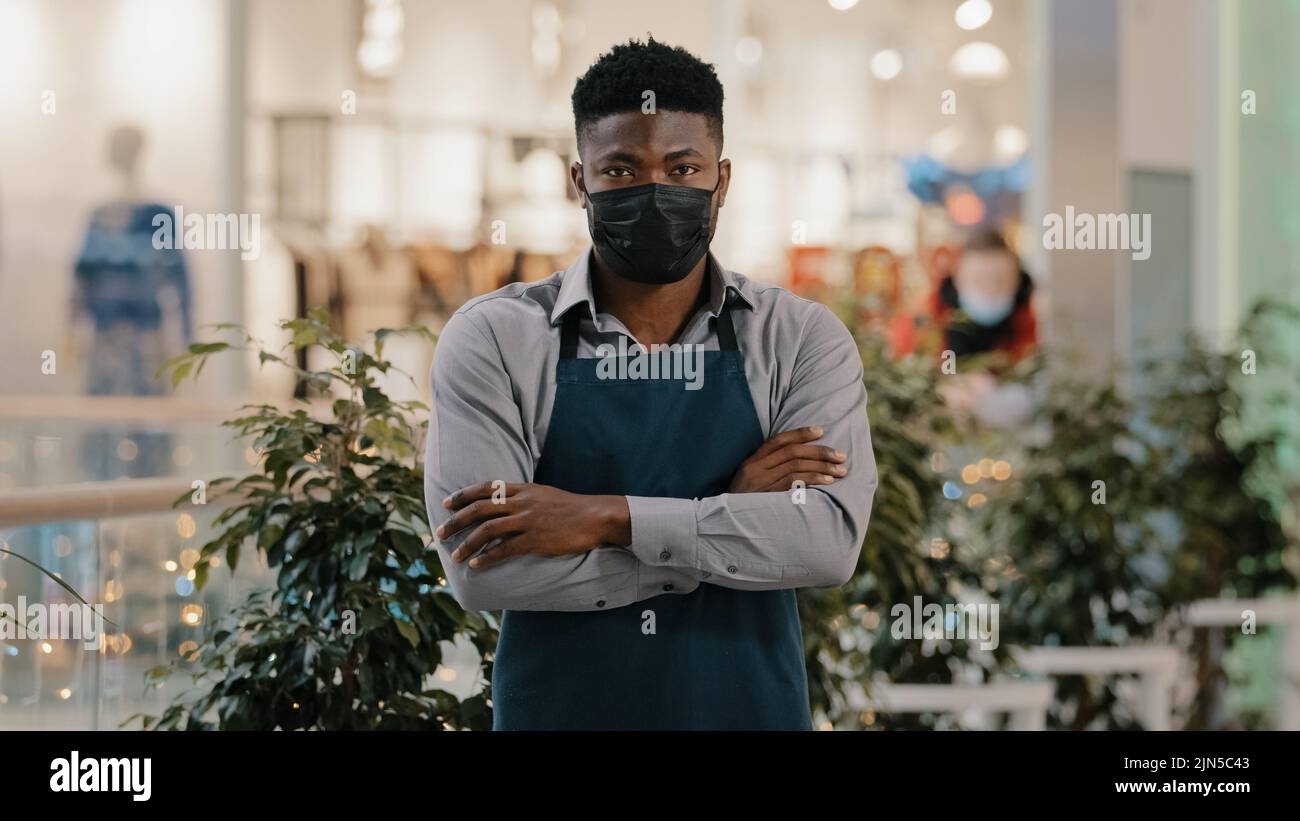 Kellner Barista Barkeeper Restaurantmitarbeiter Verkäufer trägt medizinische Maske posiert drinnen erfolgreiche selbstbewusste junge Café-Besitzer Geschäftsmann steht in Stockfoto