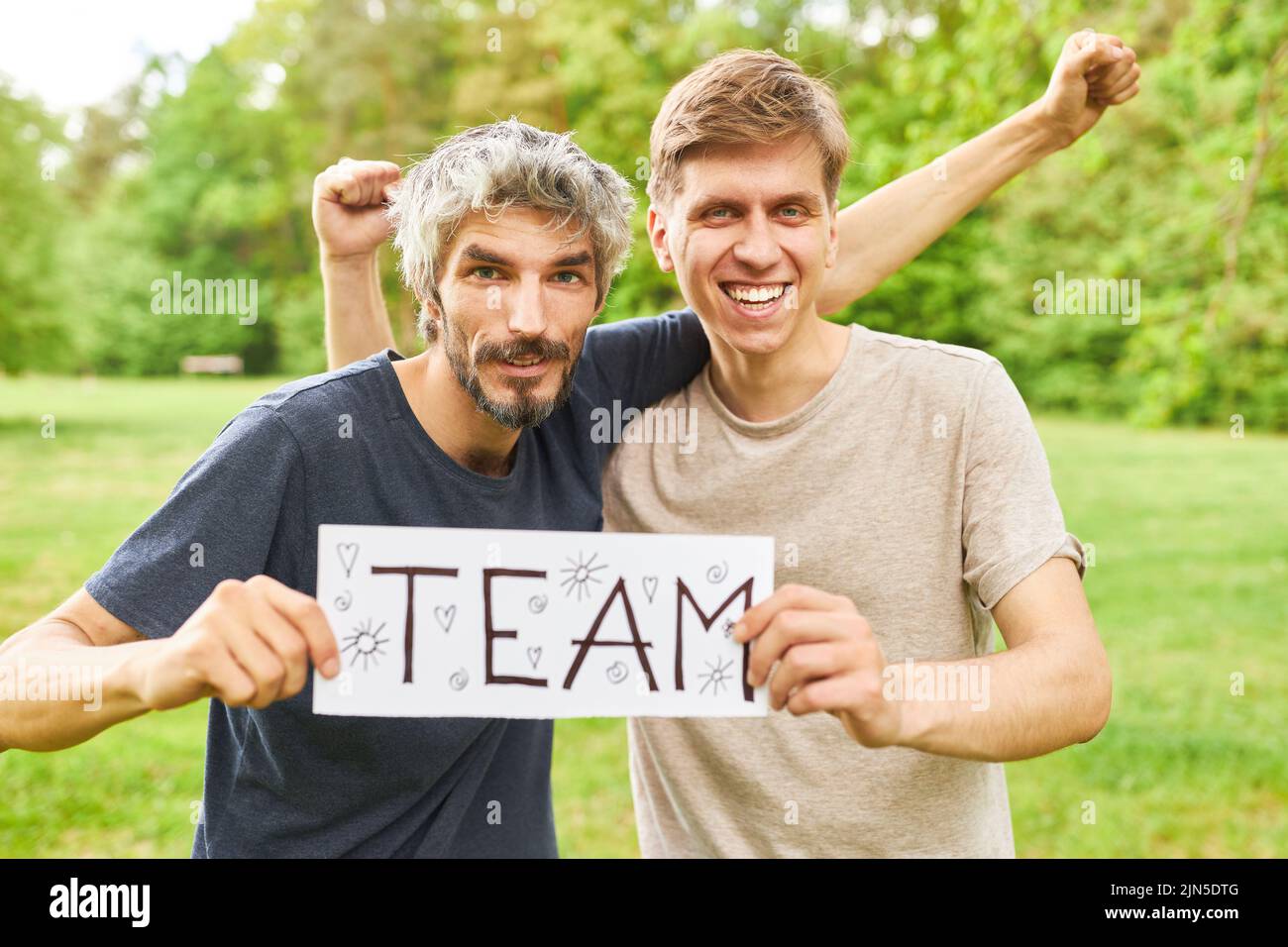 Zwei junge Männer als erfolgreiches Team halten ein Schild mit der Aufschrift Team und jubeln an Stockfoto