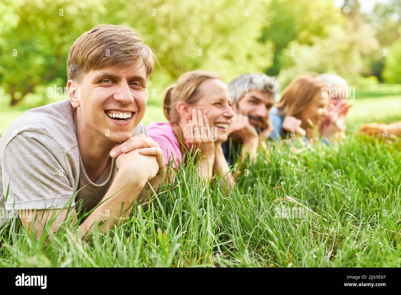 Lachender junger Mann, der im Sommer mit Freunden im Gras auf einer Wiese liegt Stockfoto