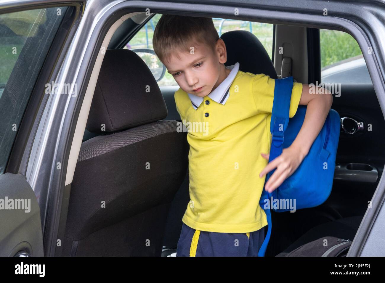 Porträt eines lächelnden Jungen mit einer Schultasche, die aus dem Auto aussteigen soll. Nach der Schule einen Schüler abholen. Der Junge steigt in das Auto. Stockfoto