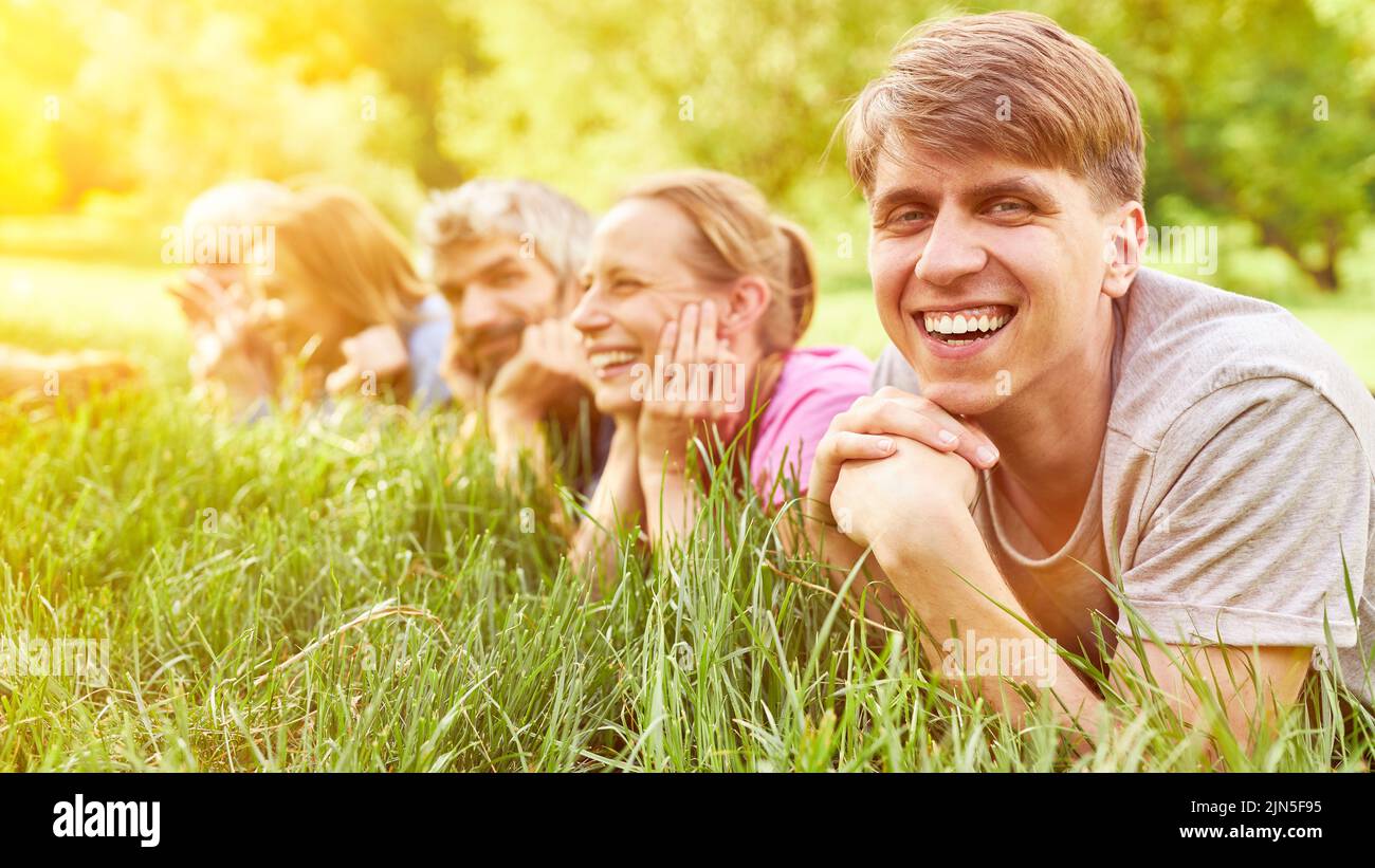 Lachender junger Mann liegt im Sommer vor einer Gruppe von Menschen auf der Wiese Stockfoto