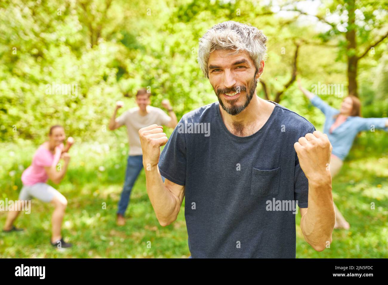 Junger Mann mit geballten Fäusten als Sieger mit seinem Team beim Outdoor-Wettbewerb Stockfoto