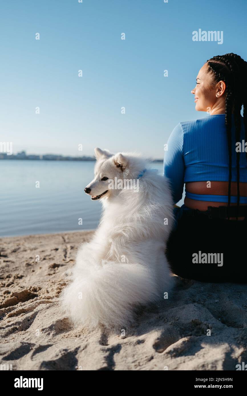 Frau mit Loks sitzt am Strand von City Lake mit ihrem besten Freund, Snow-White Dog Breed japanischen Spitz Stockfoto